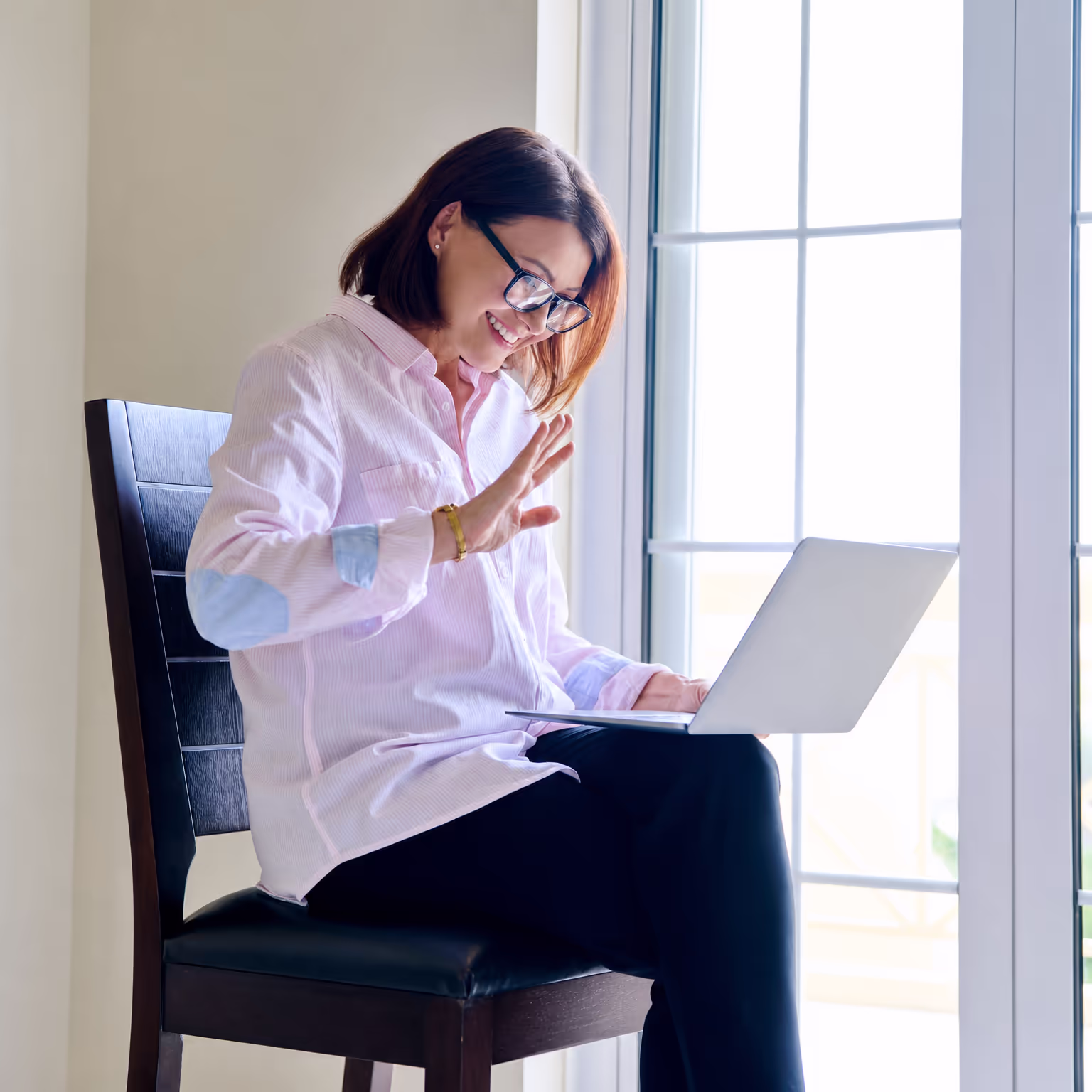 Woman smiling and waving during a telehealth video visit on her laptop
