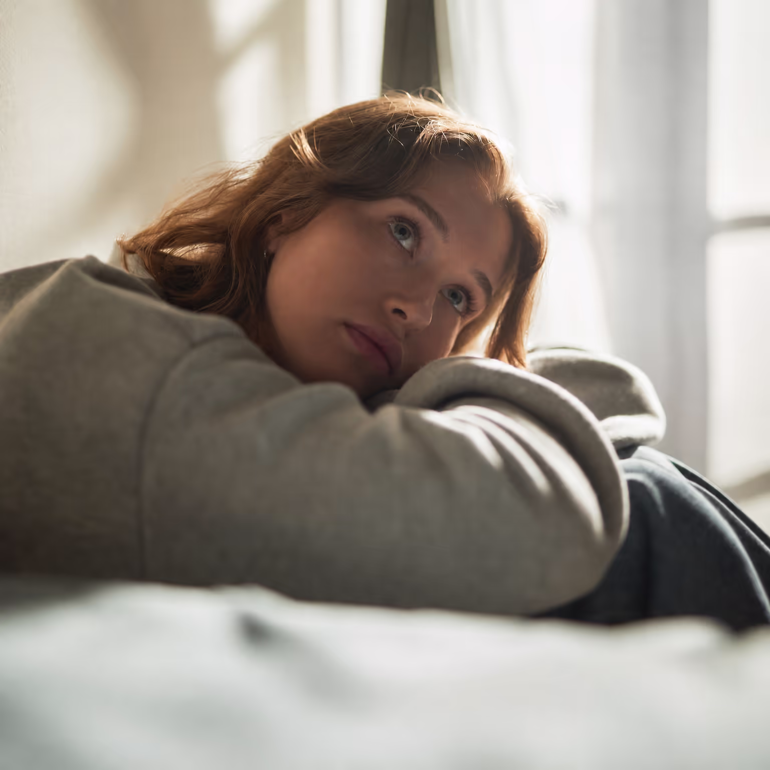 Young woman resting her head on her bed, looking tired and withdrawn