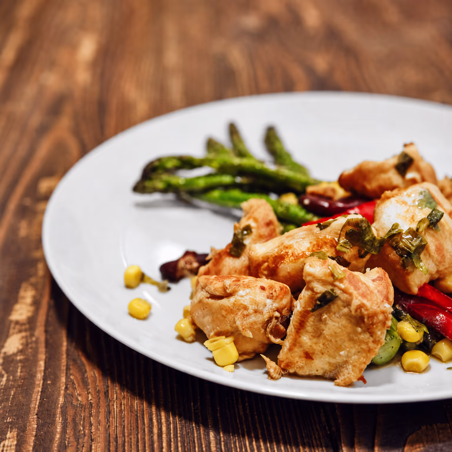 Plate of roasted chicken, asparagus and corn on a wooden table